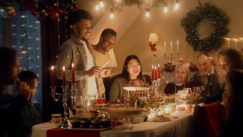 African American man cuts turkey with knife. Multi cultural family celebrating Christmas or New Year. Served holiday table with dishes and candles. Warm atmosphere of family Christmas dinner at home.