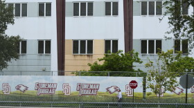 FILE - A security agent walks alongside a barrier surrounding Marjory Stoneman Douglas High School, July 5, 2023, in Parkland, Fla. Demolition of the building where 17 people died in the 2018 Parkland school shooting is set to begin, as crews will begin tearing down the three-story building at the high school on Thursday, June 13, 2024. (AP Photo/Rebecca Blackwell, File)
