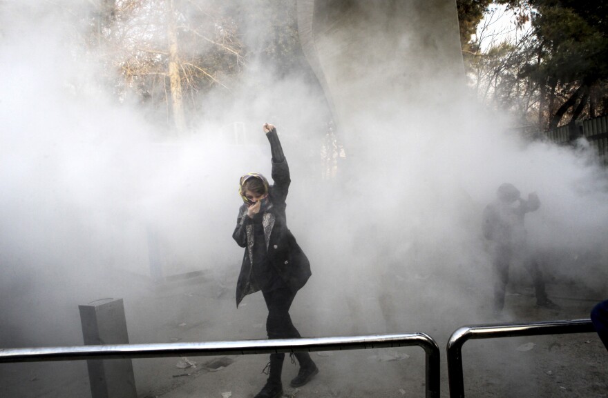 A university student takes part in a protest inside Tehran University while a smoke grenade is thrown by anti-riot Iranian police on Saturday. Iran has seen its largest anti-government protests since the disputed presidential election in 2009.