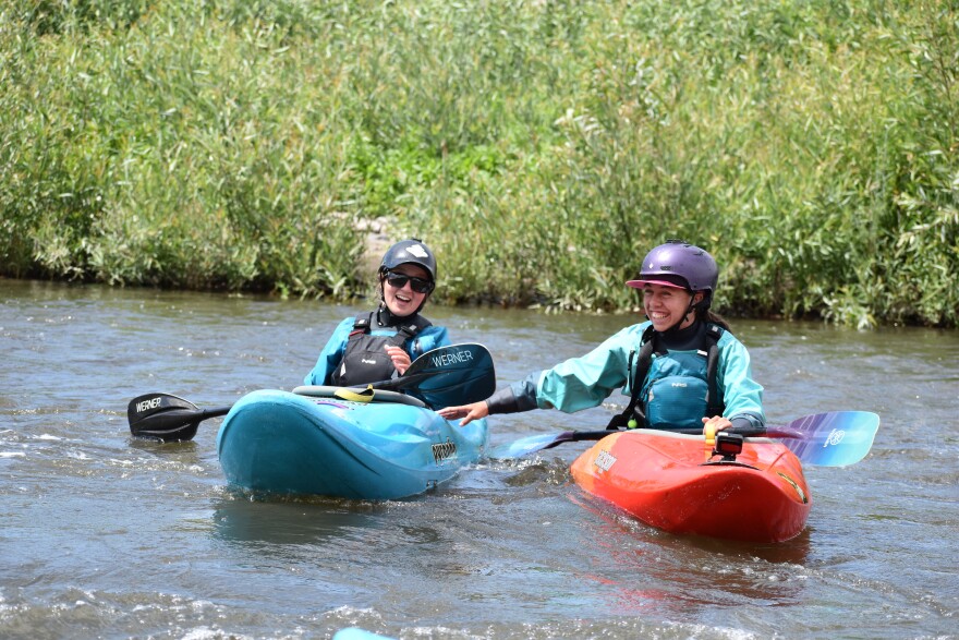 Two young kayakers smile and chat while floating side by side in calm water.
