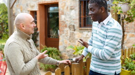 Two male farmers friendly talking outside next to wooden fence on background with brick house
