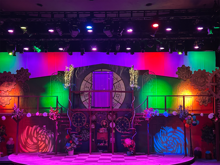 A colorful theatre set, lit up with green, orange, blue, and pink spotlights