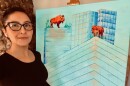 Woman, wearing glasses, poses with a painting of bison standing on buildings. 