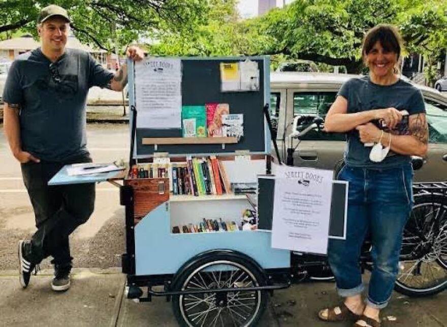 Two people in front of bike cart full of books