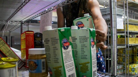 An arm reaches into metal shelves to set down a carton of broth. 