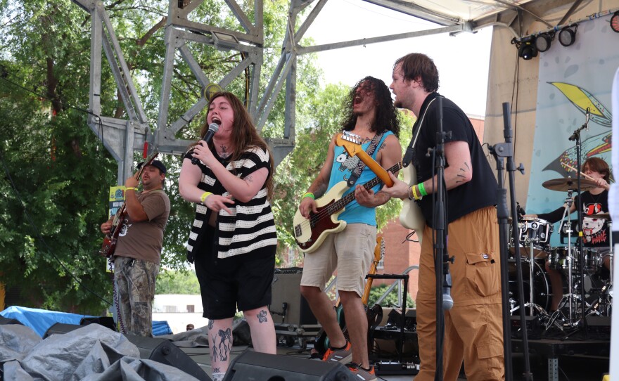 A vocalist sings into a microphone with three band members behind her.