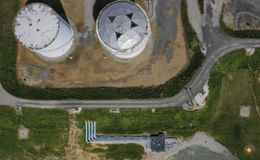 An aerial view shows two tall fuel tanks on a dirt patch, surrounded by green grass and grey roads, at Colonial Pipeline's Dorsey Junction Station in Maryland.
