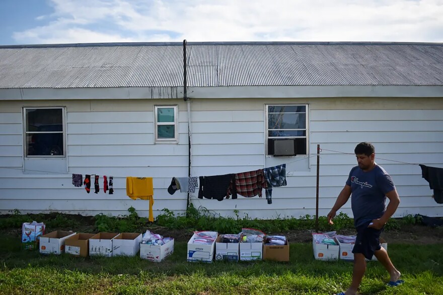 A farmworker walks past boxes of donated supplies from the Migrant Farmworkers Assistance Fund at an apple orchard just outside of Waverly, Missouri. The organization gives out donated school supplies, food, eyedrops, insulated bags for cold water, baseball caps and thin long sleeve shirts for the heat.