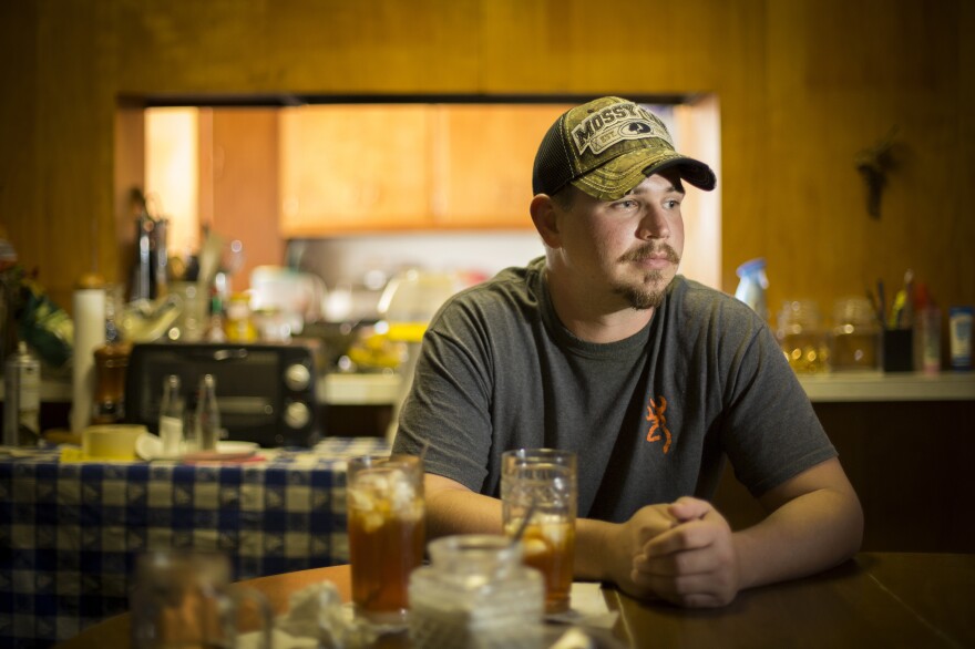 John Coffell sits at his grandmother's table in Hulen, Okla. After he hurt his back at a tire plant last year, his wages dropped so dramatically that he and his family were evicted from their home.