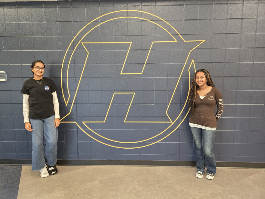 Haslett High School students Aikem Gill (left) and Nanaty Assefa (right) stand next to Haslett High School logo painted on a school wall