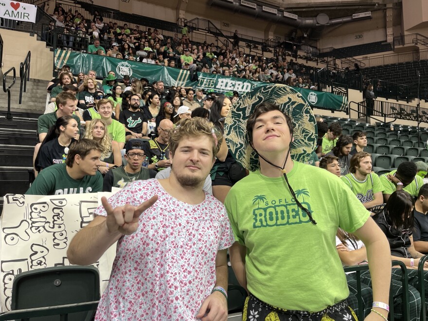 Two students in the SoFloRodeo smiling with a bunch of student fans behind them.