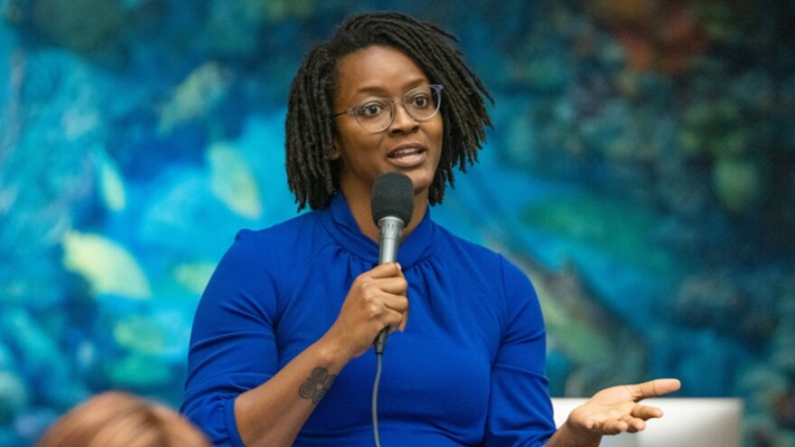 black woman in blue dress standing and talking into a microphone