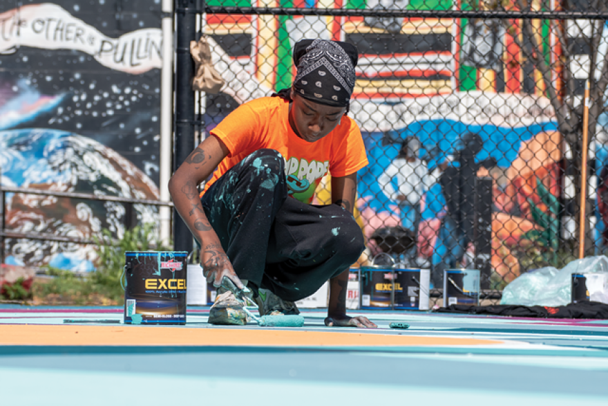 Paris Cockrell, part of the 2021 Peculiar Asphalt team, paints this year's final basketball court at the Roxie Ann Sinkler R-Center.