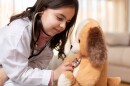 A little girl dressed as a doctor examining her teddy bear