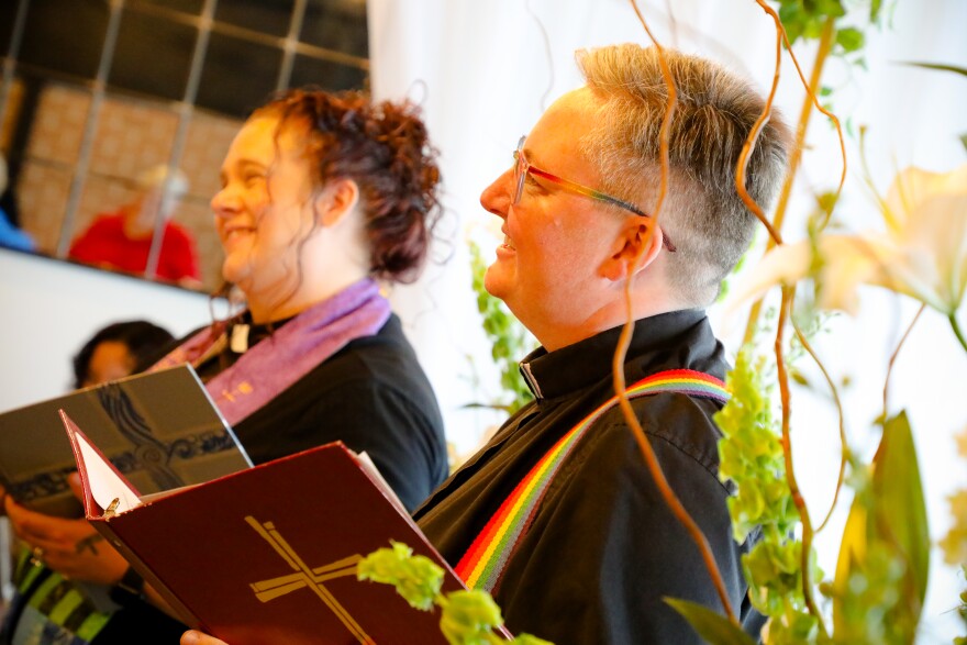 Two pastors stand with open books, prepared to officiate a wedding.