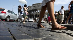 Pedestrians cross the cobblestone Via dei Fori Imperiali in front of Rome's Colosseum.