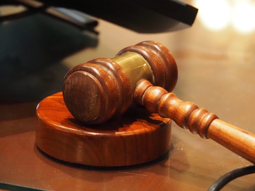 A wooden gavel resting on a stand on a wooden table.