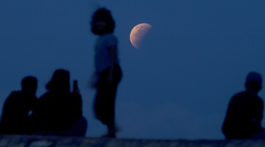 Residents watch the lunar eclipse at Sanur beach in Bali, Indonesia on Wednesday. The reddish-orange color of the super blood moon is the result of all the sunrises and sunsets in Earth's atmosphere projected onto the surface of the eclipsed moon.