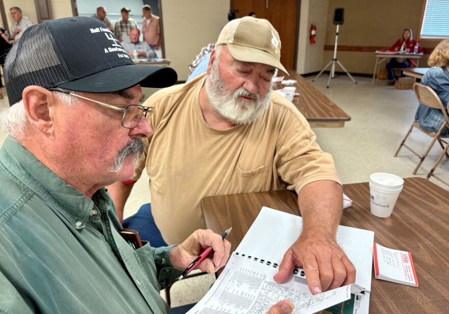 Two men are sitting at a table during a farm auction looking for farmland plot documents.
