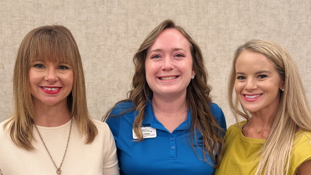 Three women in business casual attire pose with a plaque highlighting Leadership Northwest Florida Legacy for Kelsi Jackson in the middle.