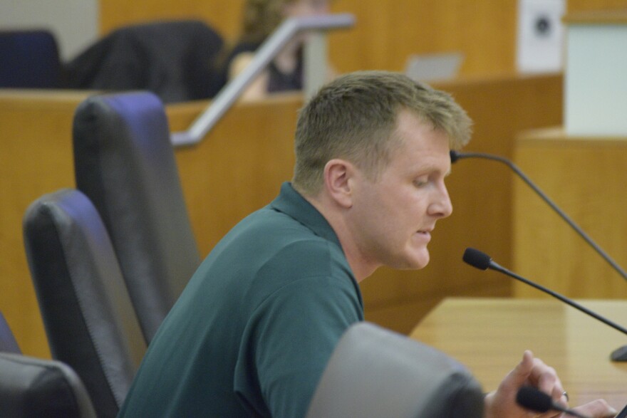 Man in green polo shirt speaks into microphone.