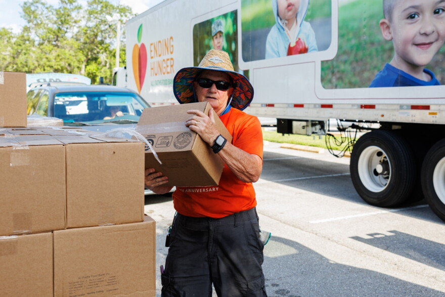 A volunteer with All Faiths Food Bank carries boxes of food during a distribution event.