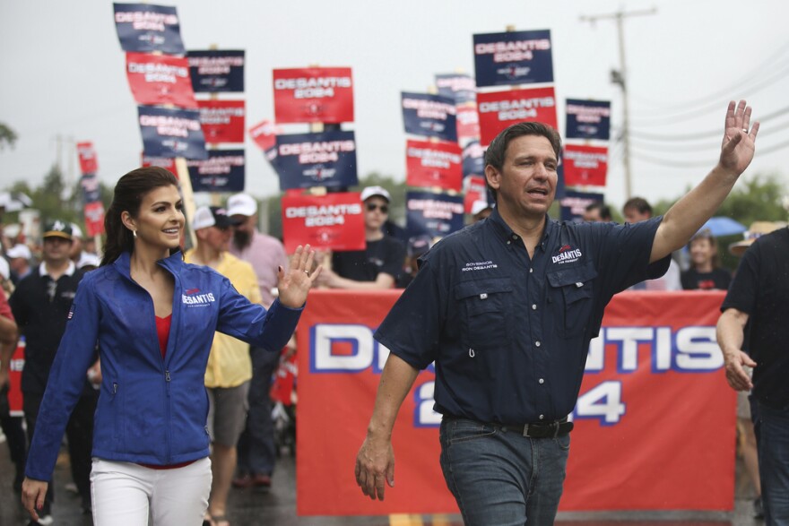 A man and a woman walk together and wave.