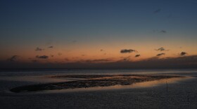 A sunset sky reflects off of water surrounding a sandbar 