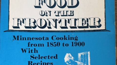 A photograph portrays a blue cookbook about Minnesota cooking from 1850-1900.