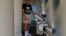 Howard Weinberg, a retired physician living with Parkinson’s disease, stands beside a stair lift at his Virginia Beach home.