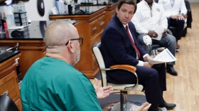 Dr. Raul Pino, left, Director of Florida Department of Health in Orange County speaks to Florida Gov. Ron DeSantis, during a discussion about opening businesses such as barber shops and nail and hair salons during at a news conference Saturday, May 2, 2020, in Orlando, Fla. (AP Photo/John Raoux)
