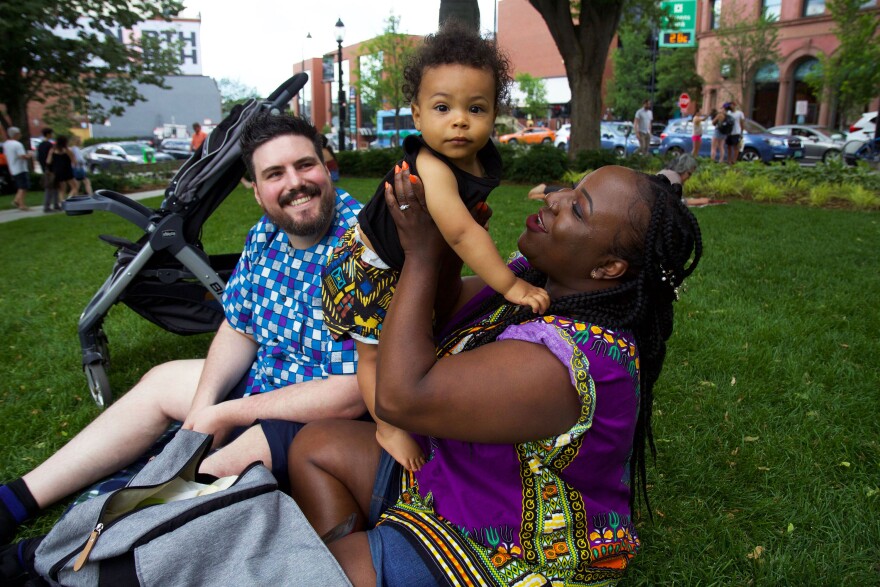 Two adults and a young child smile on a green lawn