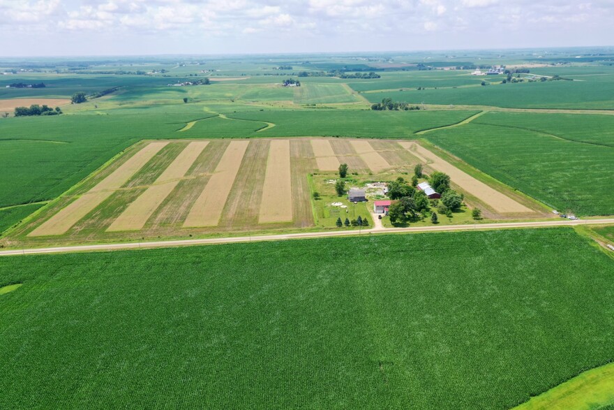 A home, barns and wide strips of brown and tan are surrounding by bright green fields.