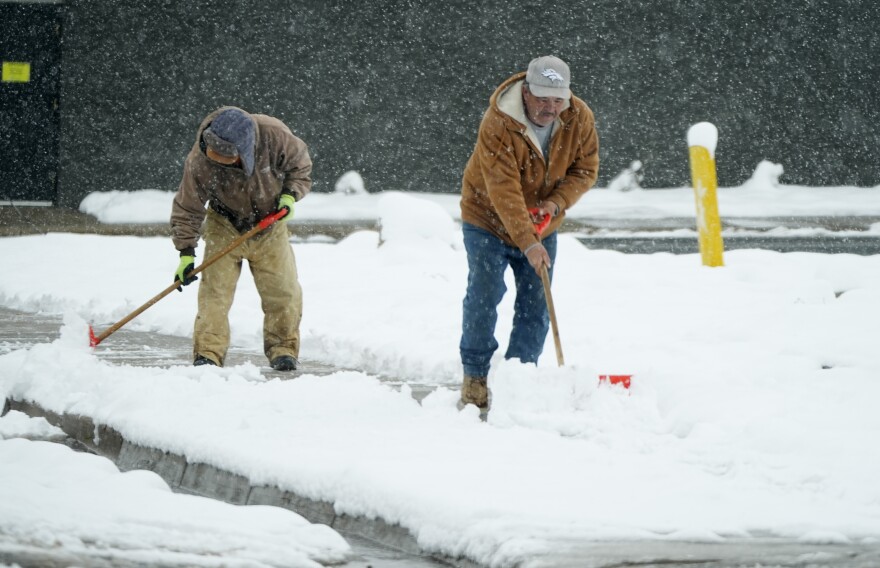 A pair of maintenance workers clear a wet layer of snow off of a walk as the remnants of the first snowstorm of the season linger, Thursday, Nov. 7, 2024, in Englewood, Colo. (AP Photo/David Zalubowski)