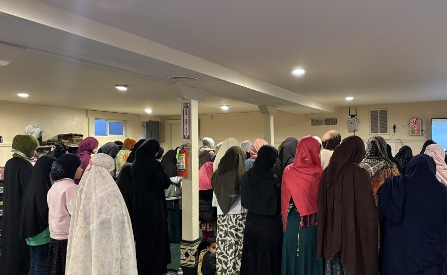 A group of women are standing in a room praying. They are all wearing headscarves. 