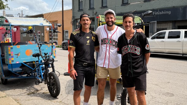 Three men pose for a photo in front of a pedicab on the street.