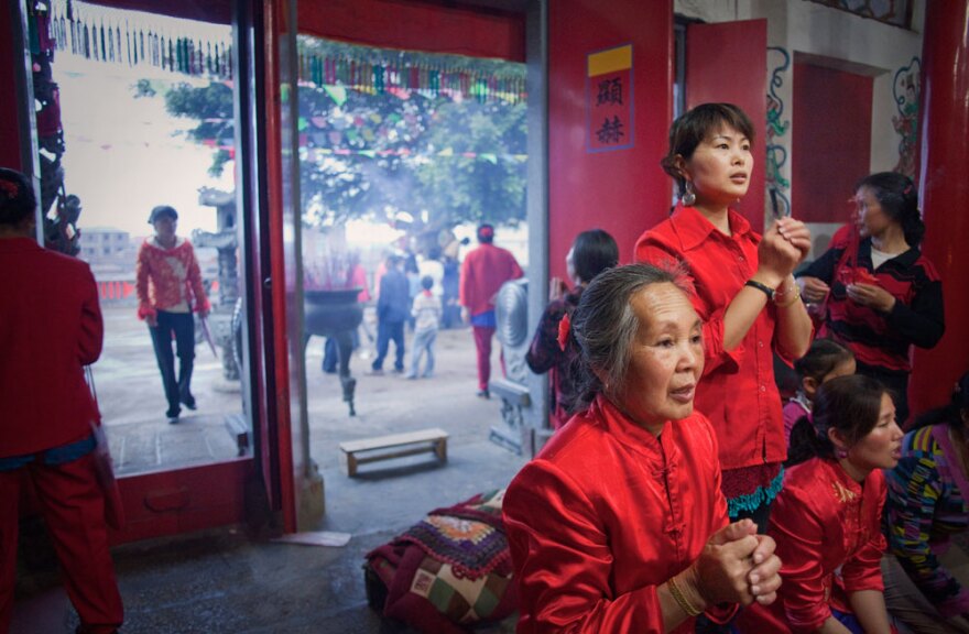 Women in lucky red outfits light incense and bow to a statue of Mazu the night before her birthday ceremony on Meizhou Island. Mazu worship is reinvigorating ancient traditions and bringing the local community together, as well as strengthening ties with Taiwan.