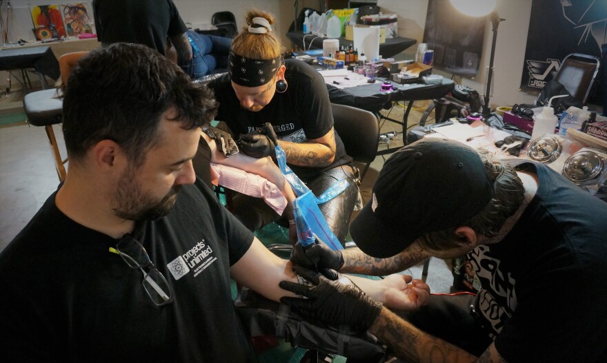 James Sercu gets a tattoo while behind him artist Will Eagle draws his 16th tattoo of the day at Drawing Dayton Together.