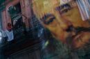 FILE - A Cuban woman hanging laundry on her balcony is seen reflected in a glass window decorated with a poster of Cuba's leader Fidel Castro in Old Havana, Cuba, Thursday, Dec. 27, 2007.