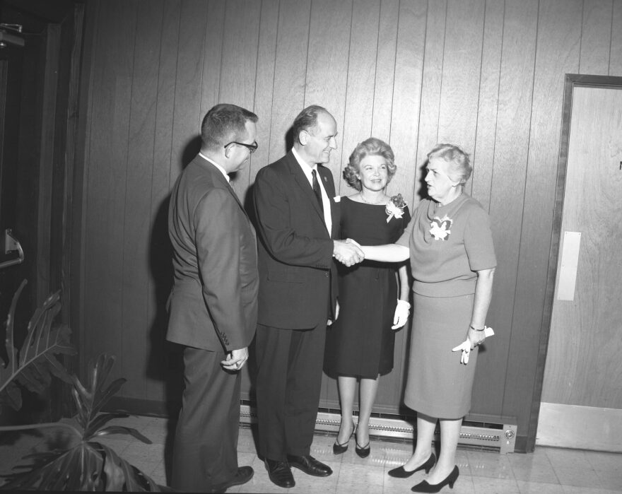 A black and white image of a man and woman shaking hands while another man and woman watch.