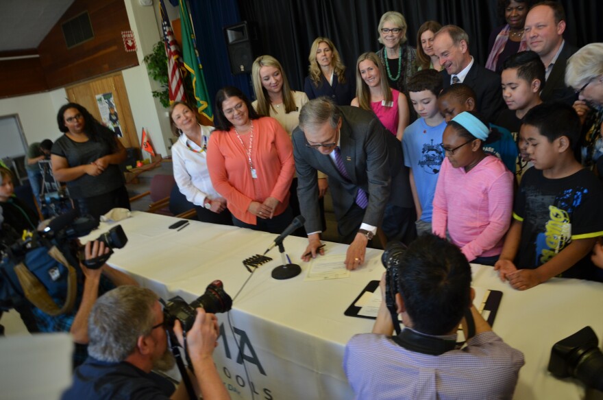 Gov. Jay Inlsee signs HB 1682 at McCarver Elementary School in Tacoma in 2016. The governor is surrounded by adults and students.