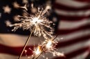 Two sparklers are lit in front of an American flag.