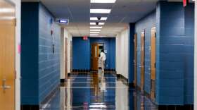A student walks in a school hallway that is otherwise empty.