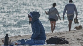 A bundled up Lucia Amato, of Argentina, sits on the shore while waiting for a friend in Miami Beach, Fla., Thursday, Jan. 29, 2026.A bundled up (AP Photo/Marta Lavandier)