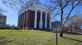 A sign in the foregrounds marks Orleans County Courthouse, while a sidewalk leads to the red-brick courthouse, with four white pillars, in the background.