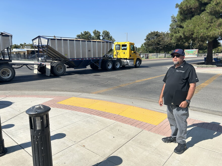 Firebaugh Mayor Freddy Valdez stands next to the intersection at Avenue 7 ½ and P Street in downtown Firebaugh on Aug. 26, 2026, as a farming truck crosses the intersection.