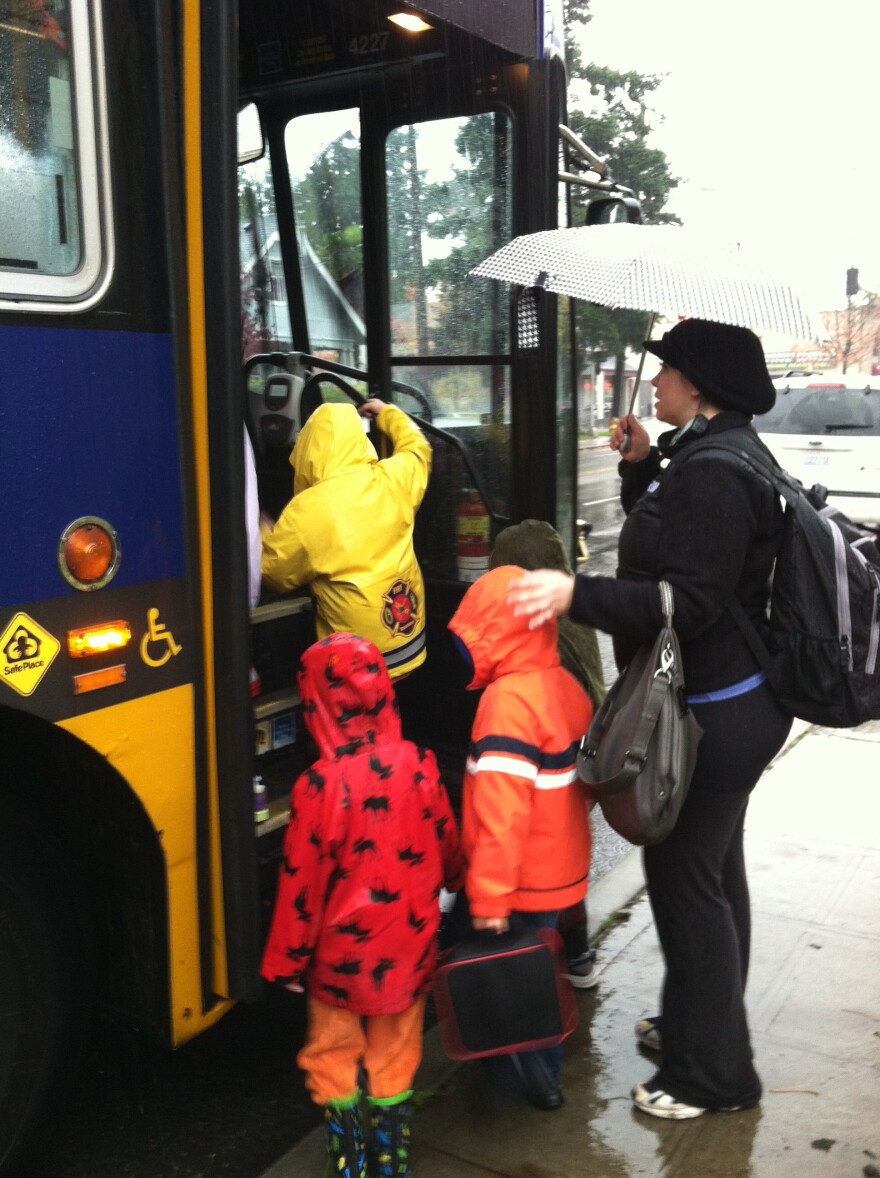 Woman with unbrella helps kids get on a bus