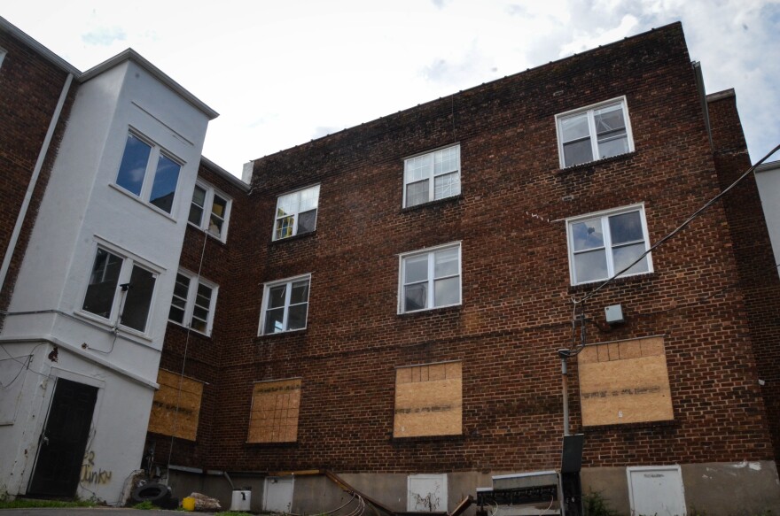 A brick apartment building has its first floor windows boarded up