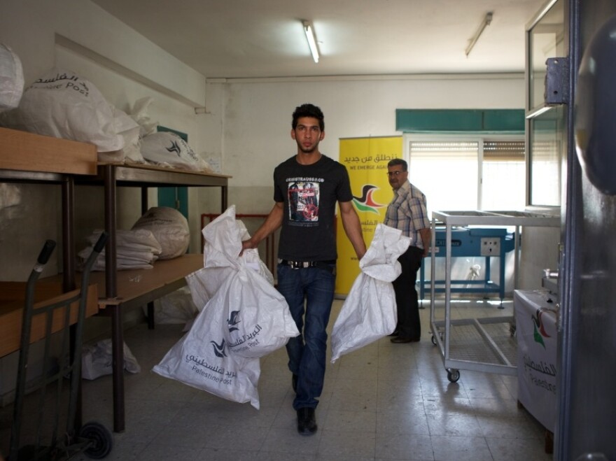 A Palestinian postal worker carries mailbags out to trucks for delivery. In advance of a possible Palestinian drive for statehood at the U.N. in September, international mail now goes through Jordan instead of Israel. The post office also has new logo and slogan: "We Emerge Again."