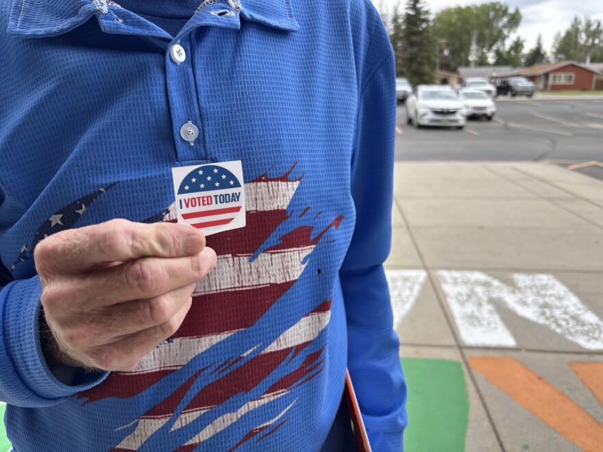 A man wearing a blue shirt with an American flag on it holds up a sticker that says “I voted today.”
